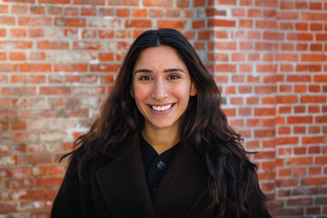 En person som smiler foran en murvegg