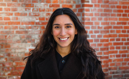 En person som smiler foran en murvegg En person som smiler foran en murvegg