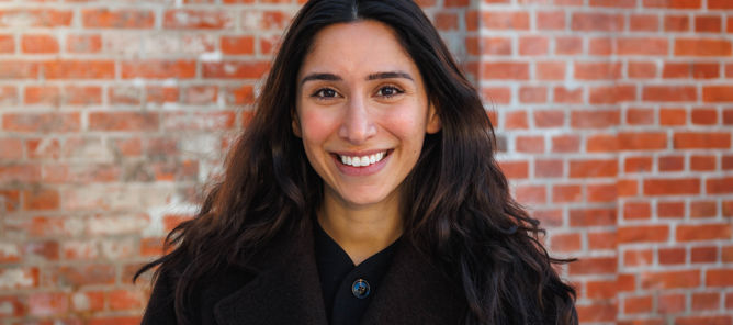 En person som smiler foran en murvegg En person som smiler foran en murvegg