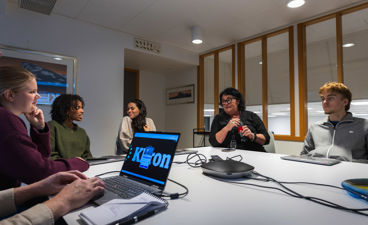 en gruppe mennesker som sitter rundt et bord med en bærbar PC